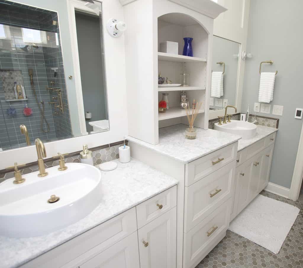 Elegant bathroom remodeling project by a bathroom remodeling contractor, featuring double sinks with gold fixtures, custom white cabinetry, marble countertops, and a stylish walk-in shower with blue tiles.