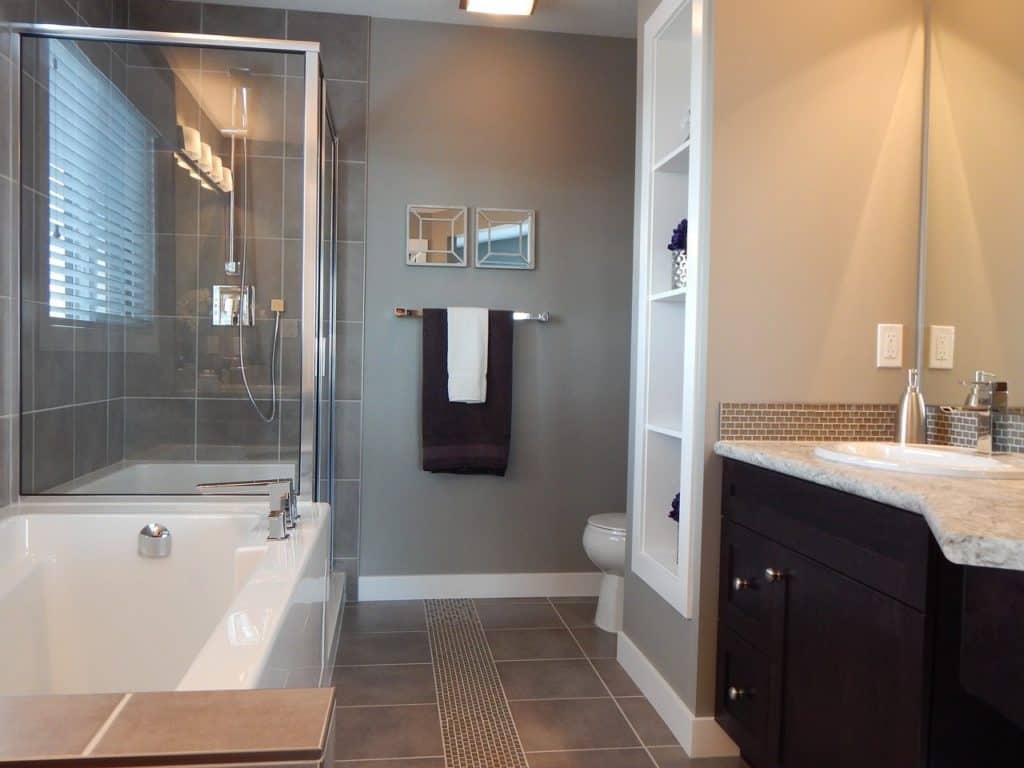 Bathroom remodeling contractor project featuring a modern bathroom with a glass-enclosed shower, white bathtub, and dark wood vanity.