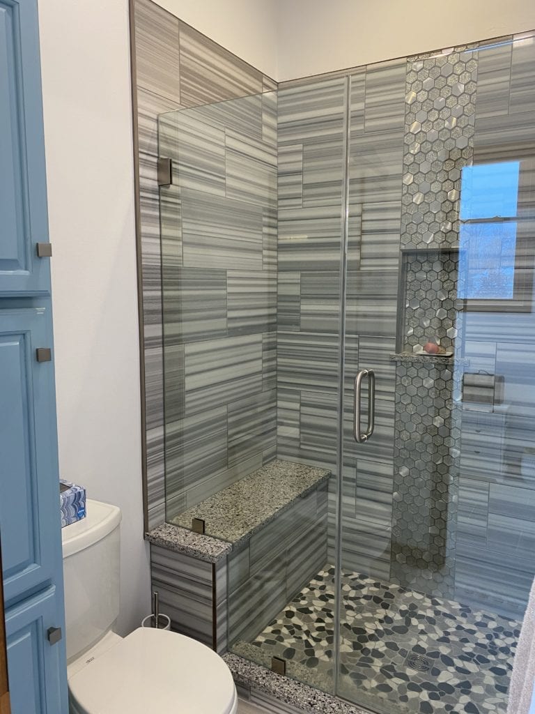 Modern bathroom remodeling contractor project featuring a stylish glass-enclosed shower with geometric tile design and custom blue cabinetry.